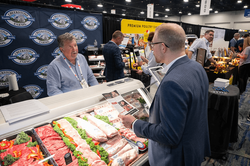 Utstillere og deltakere diskuterer kjøttprodukter ved en messestand under Den årlige kjøttkonferansen