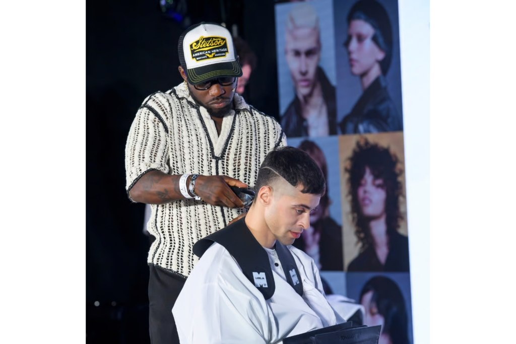 Stylist som utfører en direktedemonstrasjon av en hårklipp på scenen under Salon International