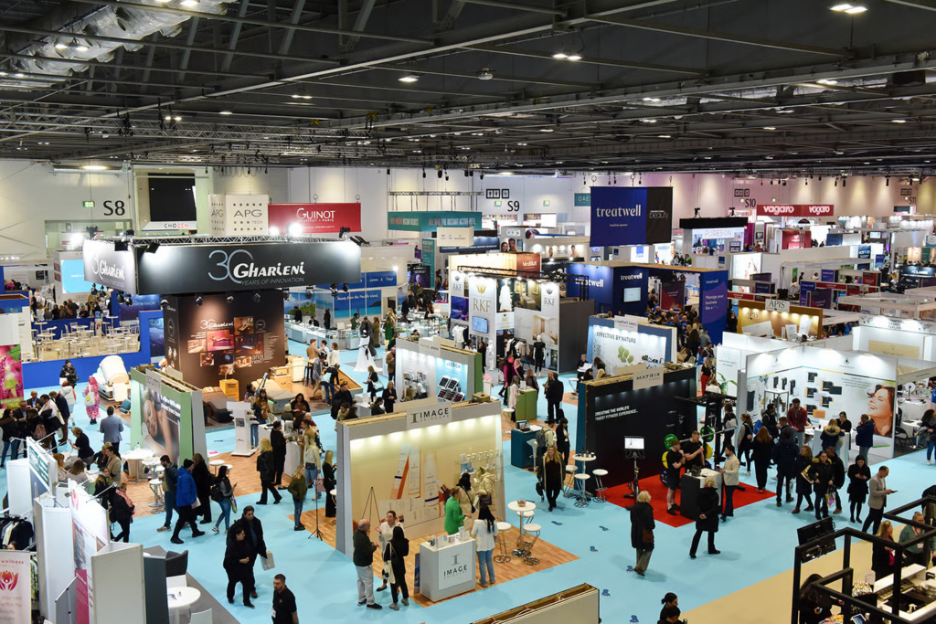 Oversiktsbilde av en travel utstillingshall på en skjønnhetsmesse med merkevareboder og folkemengder på Professional Beauty London
